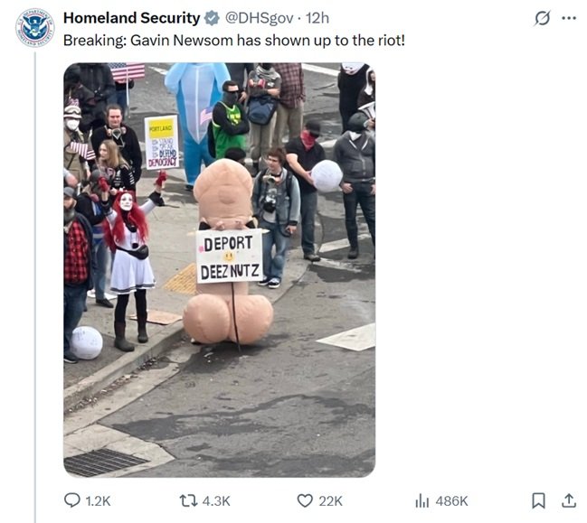 Protesters gather at a rally, featuring a humorous costumed figure holding a sign that reads "DEPORT DEEZ NUTZ" amidst a crowd.