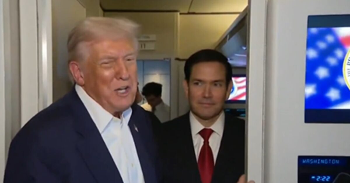 Donald Trump speaks while Marco Rubio stands nearby on an airplane, with an American flag visible in the background.
