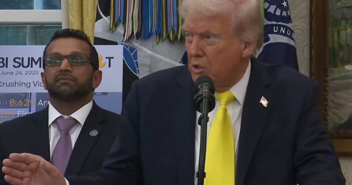 Donald Trump speaking at a podium in the Oval Office, with an official in a suit standing beside him, discussing the upcoming FBI Summit.