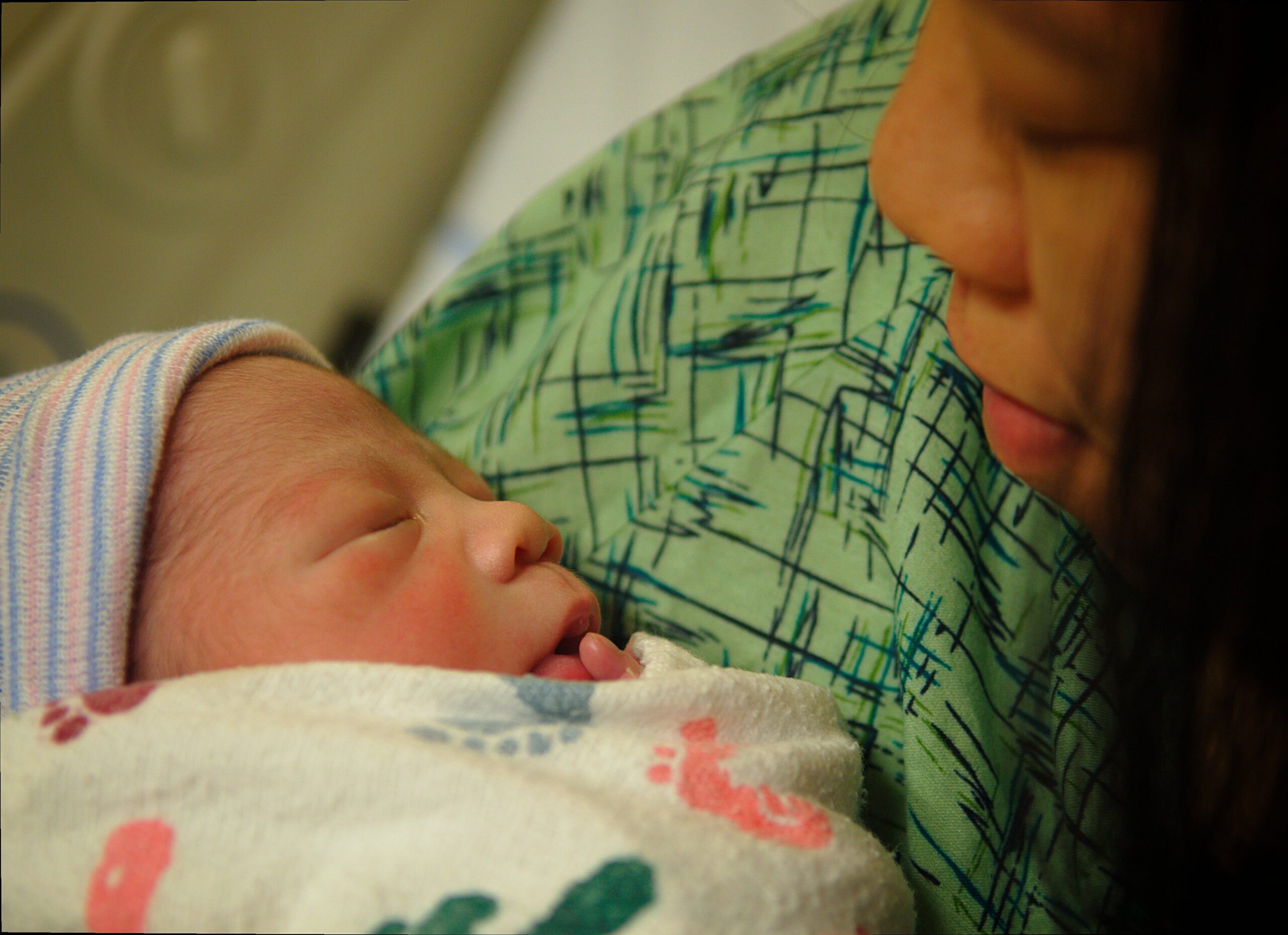 Newborn baby peacefully sleeping in a hospital blanket while being cradled by a caregiver, showcasing a tender moment of connection.