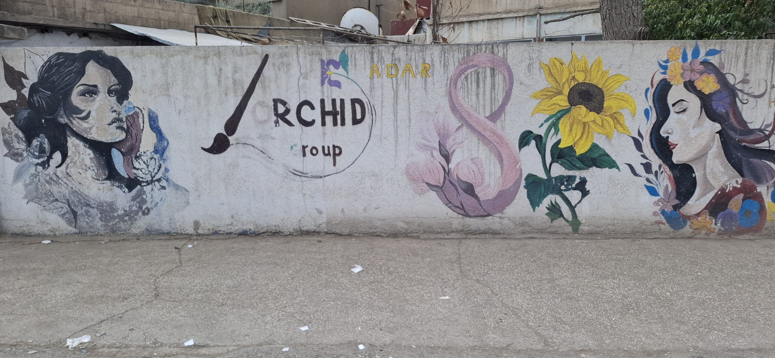 Colorful street mural featuring two portraits of women, a sunflower, and the text "Orchid Group," showcasing urban art and creativity.