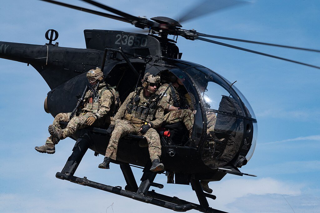 Military helicopter in flight with soldiers onboard, showcasing tactical gear and operational readiness against a clear blue sky.