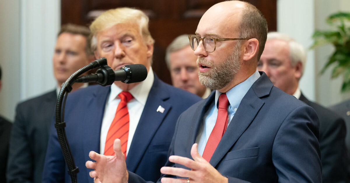 A speaker addresses an audience while Donald Trump listens attentively during a press event in the White House, highlighting key policy discussions.