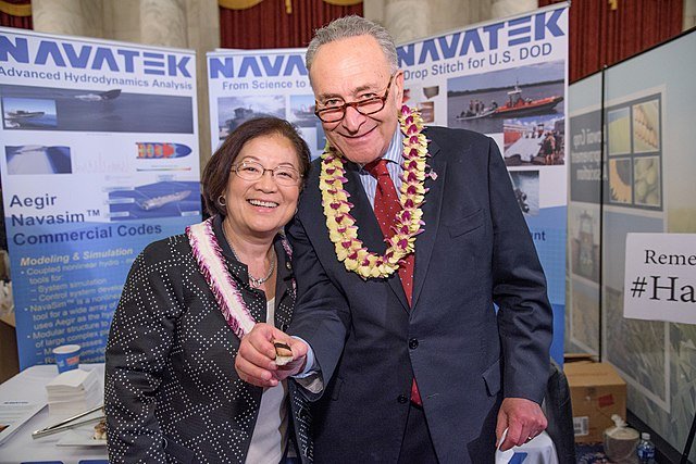 Smiling individuals at a NAVATEK booth, showcasing advanced hydrodynamics analysis and modeling, with promotional materials in the background.
