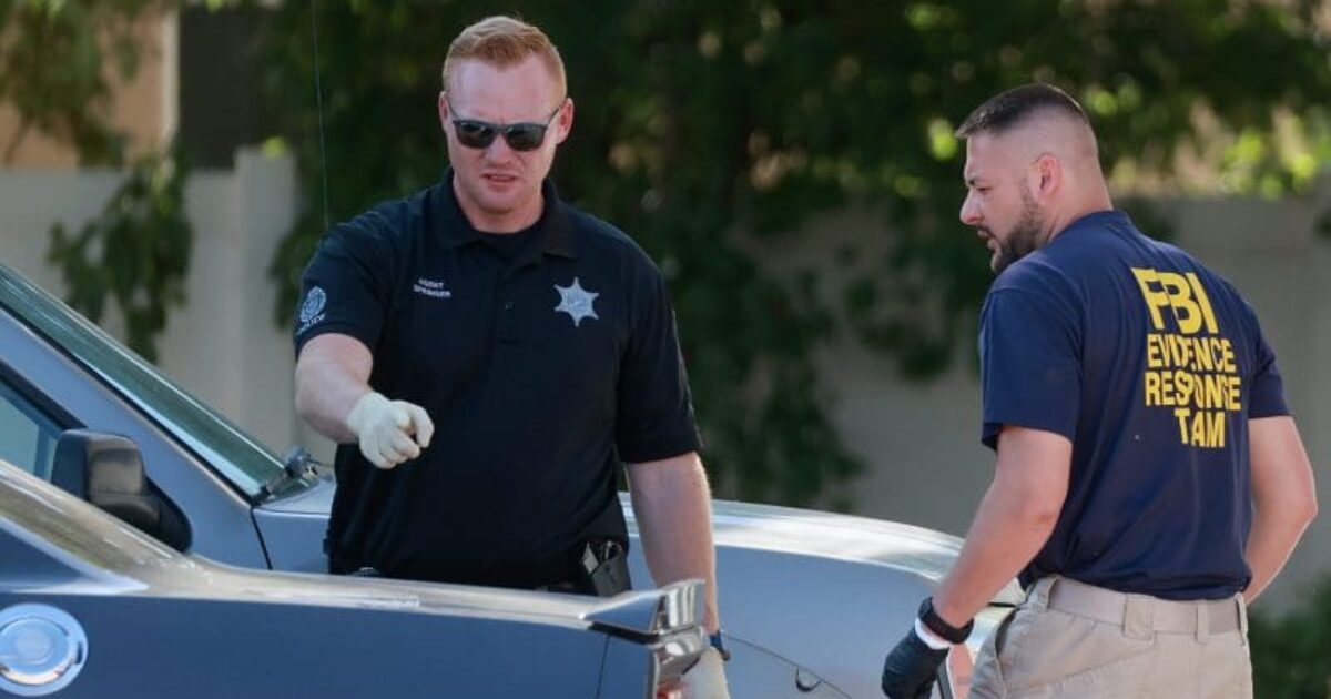 Two law enforcement officers, one in a sheriff's uniform and the other in an FBI Evidence Response Team shirt, examining a vehicle at a crime scene.