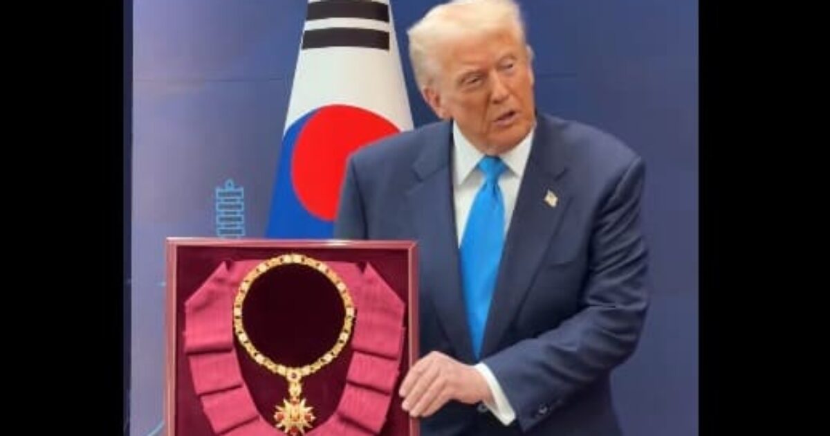 Donald Trump presents a ceremonial necklace displayed in a case, alongside the South Korean flag, at an official event.
