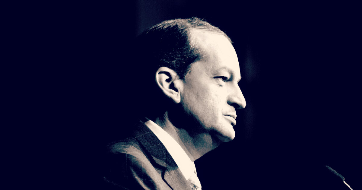 Profile of a man in a suit speaking at a podium, captured in a dramatic black and white style.