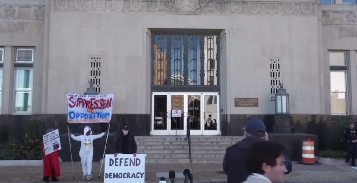 Protesters holding signs advocating for democracy and opposing suppression gather outside a government building, highlighting civic engagement and activism.