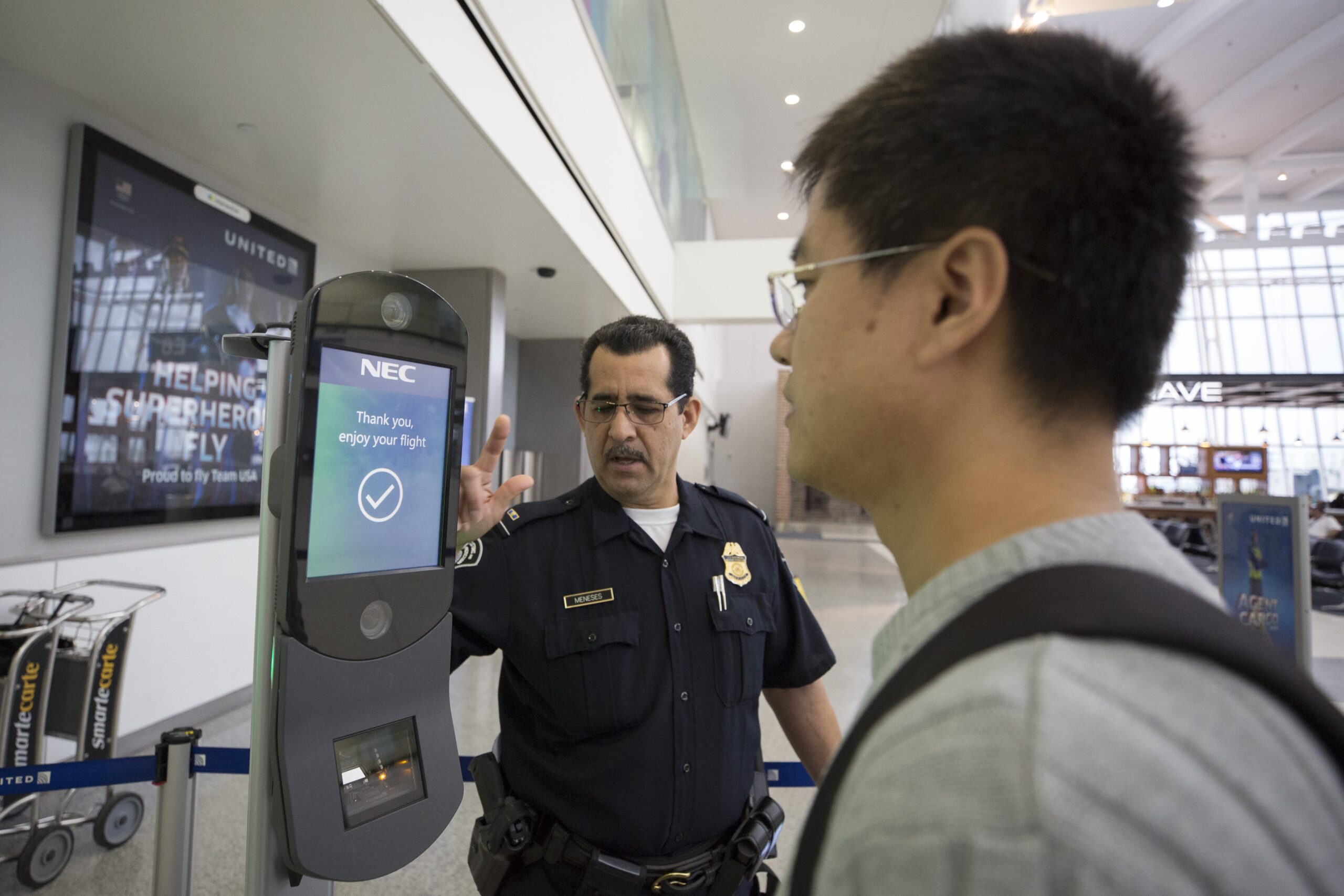 Airport security officer assisting a traveler at a self-service kiosk displaying a flight confirmation message.