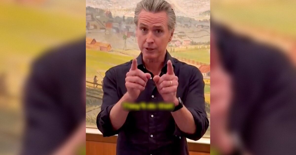 Man gesturing with hands while speaking, set against a colorful landscape painting in the background.