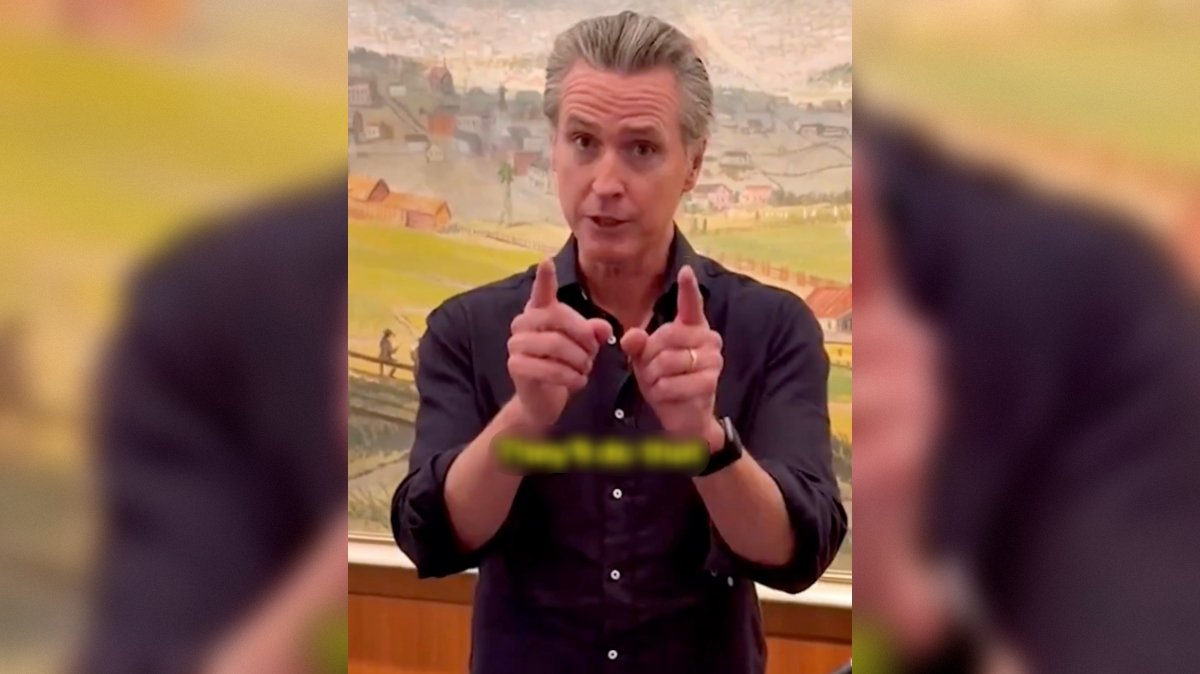 Man gesturing with hands while speaking, set against a colorful landscape painting in the background.