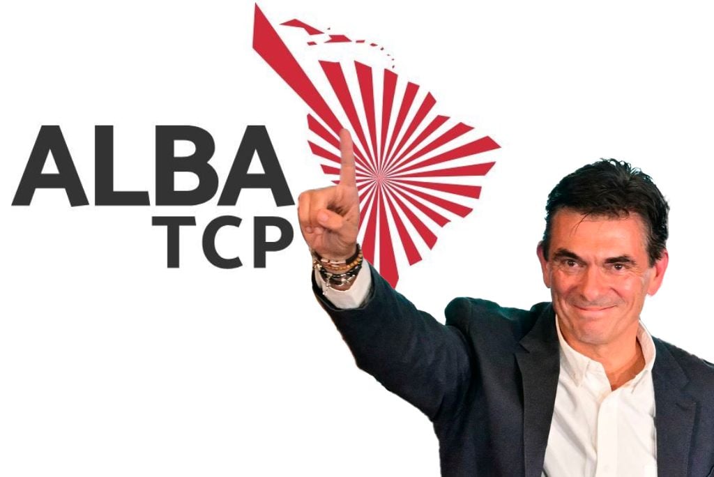 Man in a suit raising a finger in front of the ALBA TCP logo, symbolizing political support and engagement in regional cooperation.