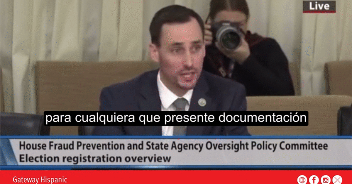 A speaker presents on election registration and fraud prevention at a policy committee meeting, while a photographer captures the event in the background.
