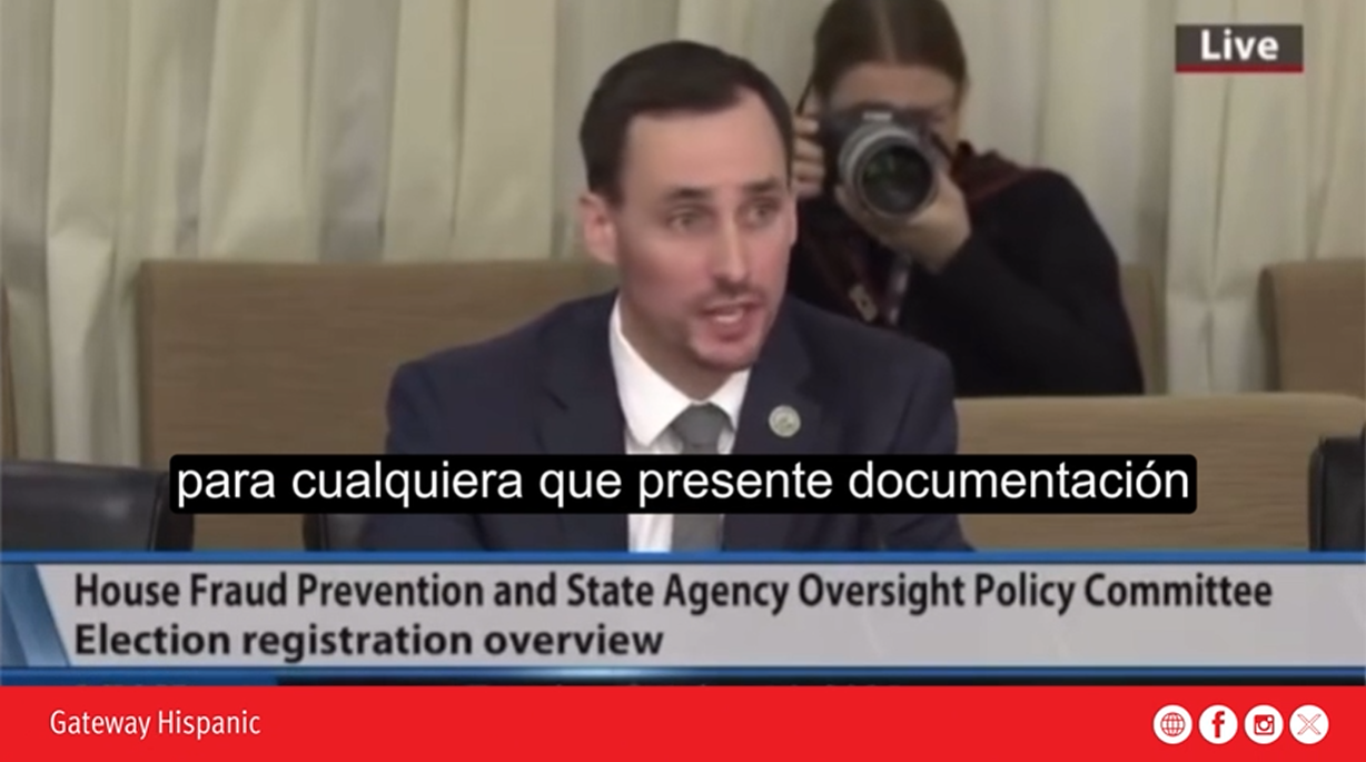 A speaker presents on election registration and fraud prevention at a policy committee meeting, while a photographer captures the event in the background.