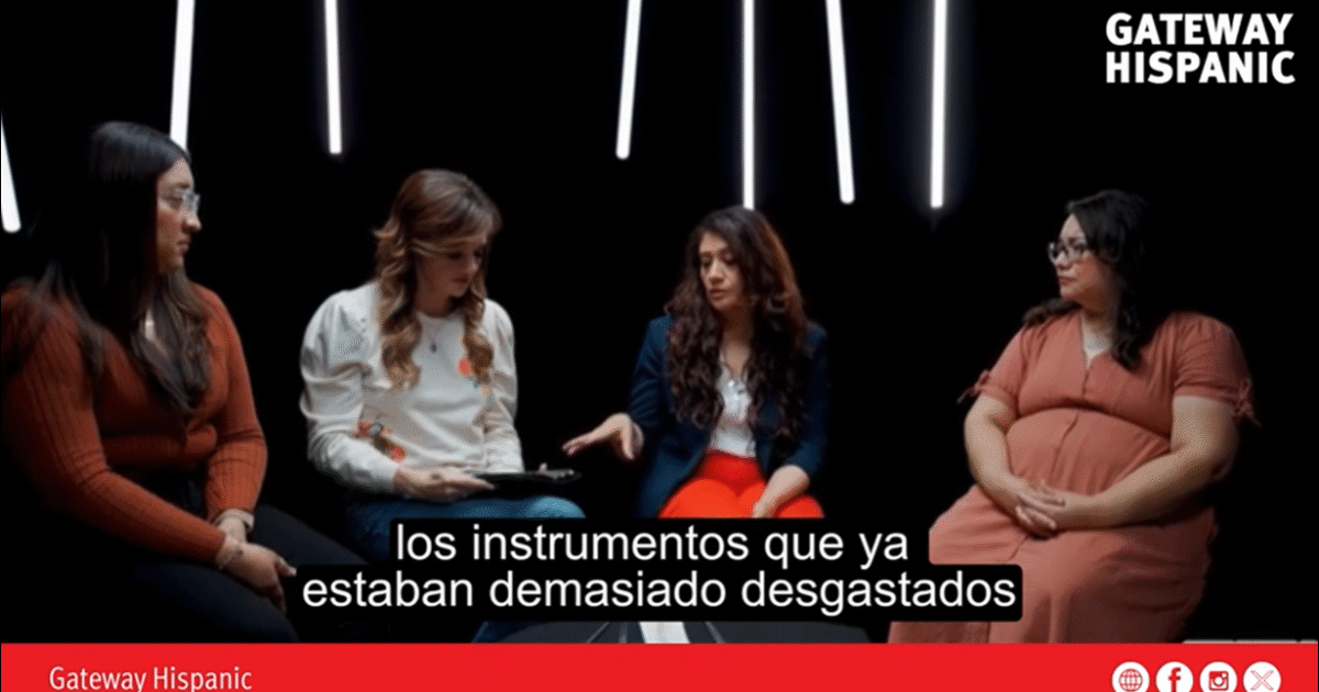 Four women engaged in a discussion about well-used instruments, set against a dark background with dramatic lighting.