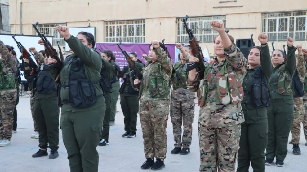 Women in military attire raising fists and holding rifles in a display of solidarity during a training or rally event.