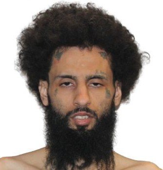 Portrait of a man with curly hair and a full beard, featuring visible facial tattoos, against a plain white background.
