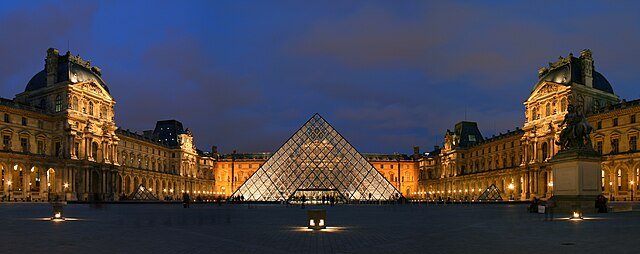 Louvre Museum at dusk, featuring the iconic glass pyramid surrounded by historic architecture and illuminated pathways.