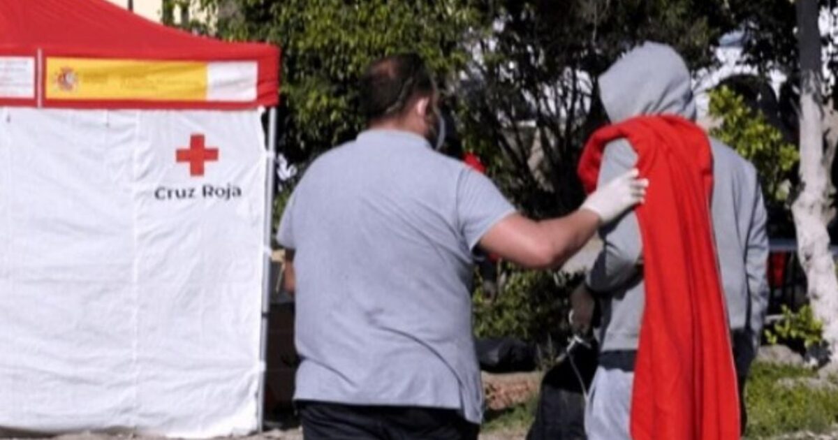 Volunteer assisting individual in need at Cruz Roja emergency aid station outdoors.