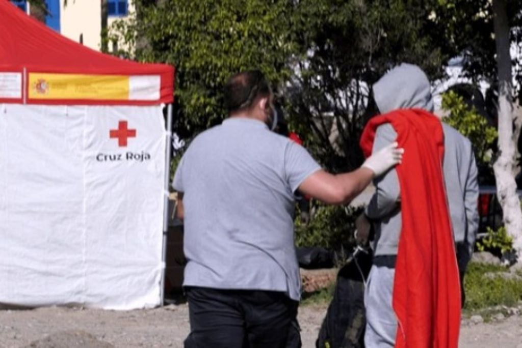 Volunteer assisting individual in need at Cruz Roja emergency aid station outdoors.