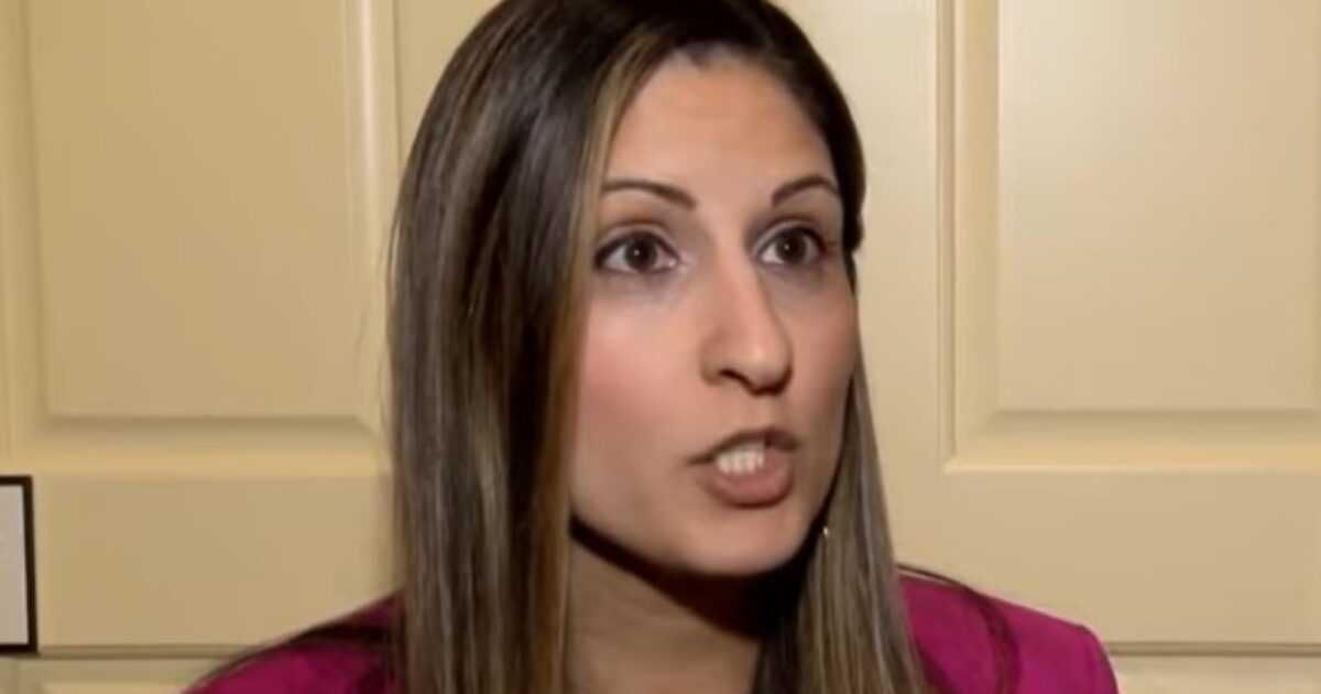 Woman with long hair speaking passionately in a professional setting, wearing a pink blazer against a light-colored background.