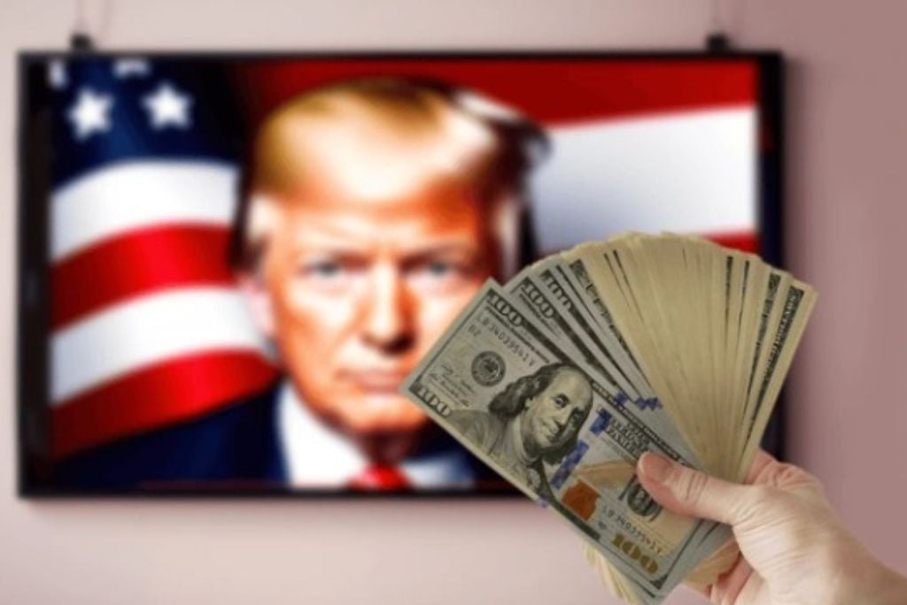 Hand holding cash in front of a television displaying an image of a person with an American flag background.