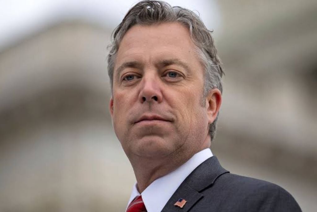 Portrait of a man in a suit with a red tie and American flag pin, standing confidently outdoors.