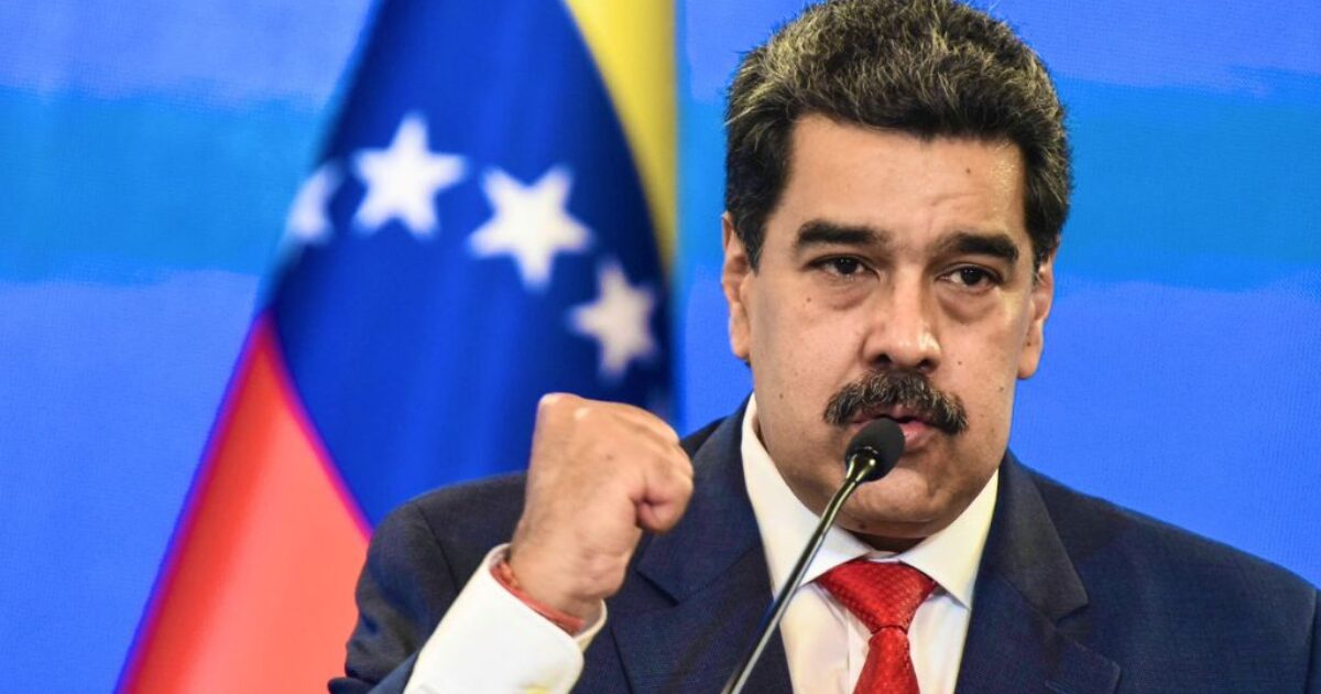 Venezuelan President Nicolas Maduro delivers a speech with a raised fist, emphasizing his message against a backdrop of the Venezuelan flag.