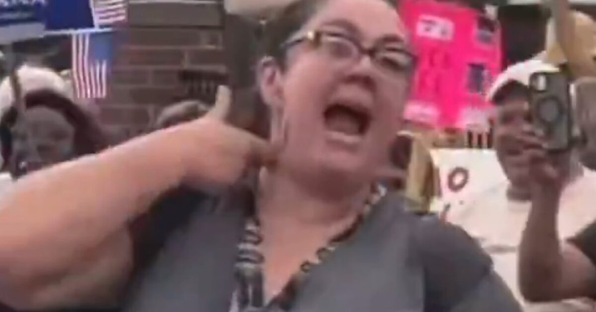 Protester passionately expressing her views at a rally, surrounded by supporters holding signs and flags.