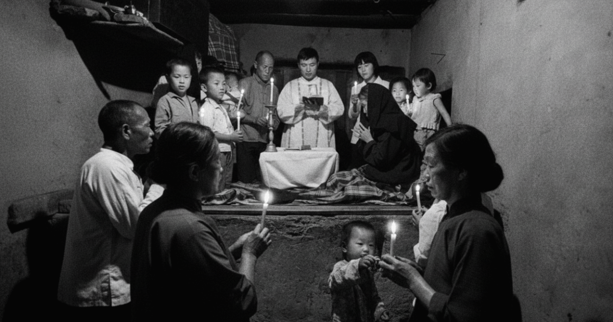 A group of people of various ages participate in a candlelit ceremony in a dimly lit room, creating a solemn and communal atmosphere.