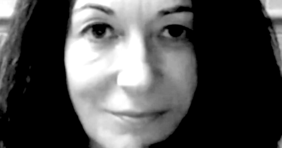 Close-up portrait of a woman with dark hair and a neutral expression, captured in black and white.