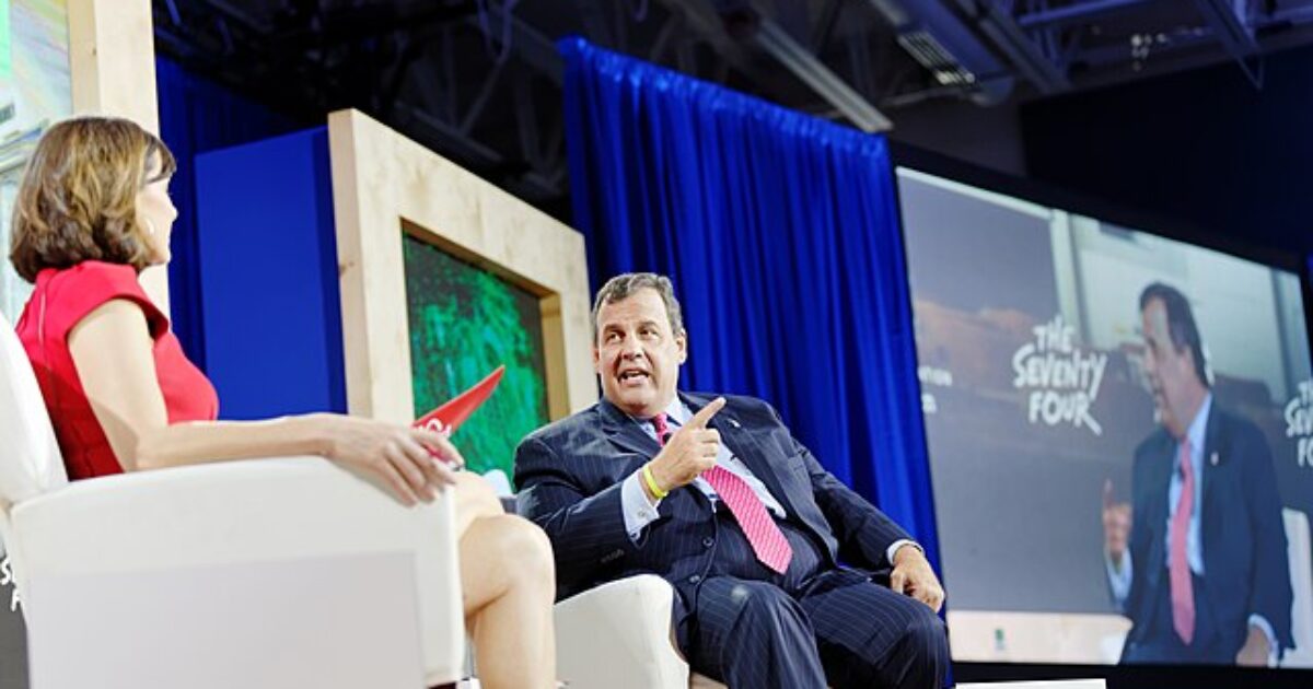 Panel discussion featuring a man and a woman engaged in conversation on stage, with a large screen displaying the event title in the background.