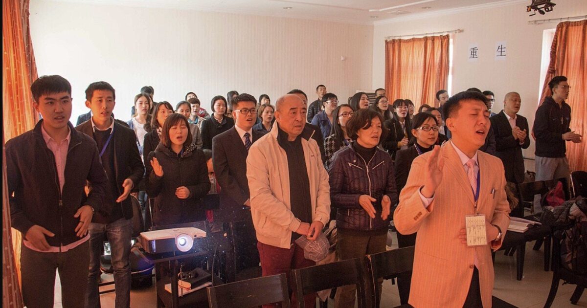 A diverse group of people engaged in a worship service, singing and expressing devotion in a bright, indoor setting.