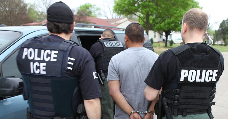 Law enforcement officers in tactical gear apprehending an individual during an immigration enforcement operation.