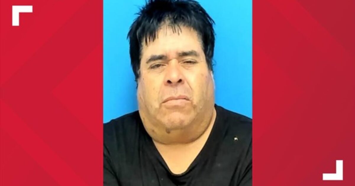 Mugshot of a middle-aged man with dark hair and a serious expression against a blue background.