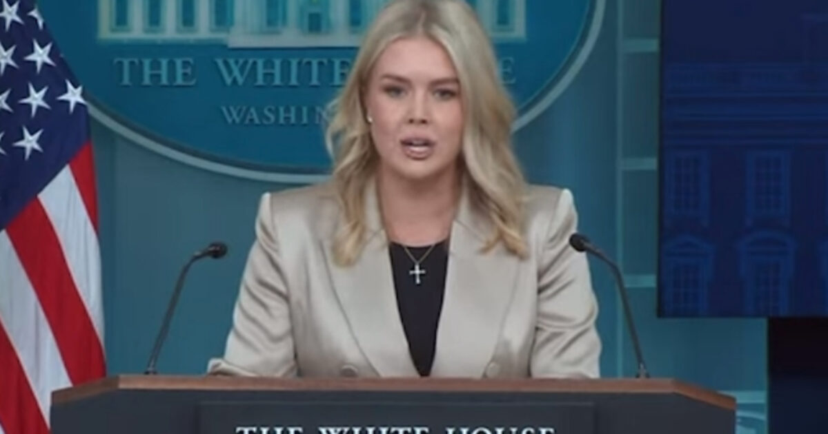 White House press briefing featuring a speaker in a light-colored blazer addressing the media with the U.S. flag in the background.