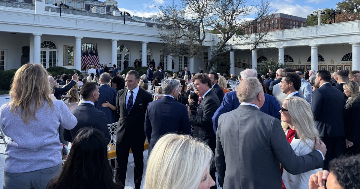 Crowd of attendees mingling at a formal outdoor event at the White House, featuring prominent guests and U.S. flags in the background.