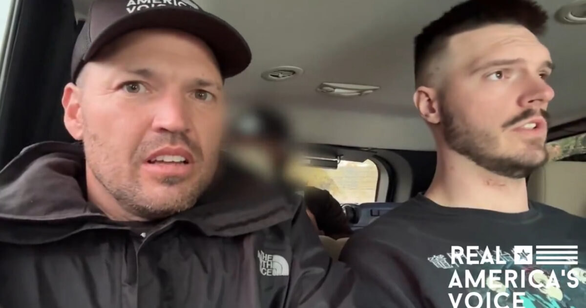 Two men with concerned expressions sitting inside a vehicle, discussing an important topic, with a blurred figure in the background.