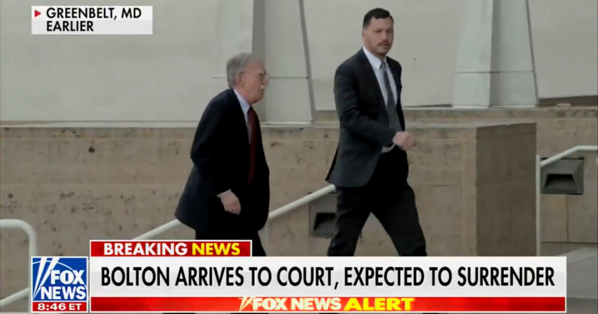 John Bolton arrives at a courthouse in Greenbelt, Maryland, accompanied by security, expected to surrender.