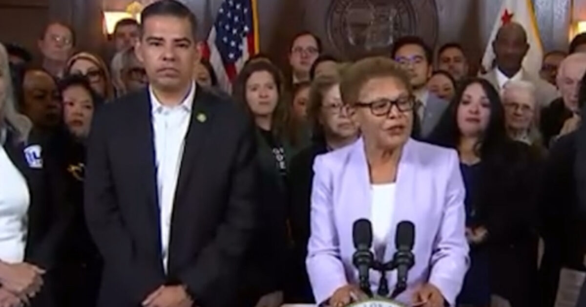 Political leaders addressing an audience during a press conference, with flags in the background and a diverse group of supporters behind them.