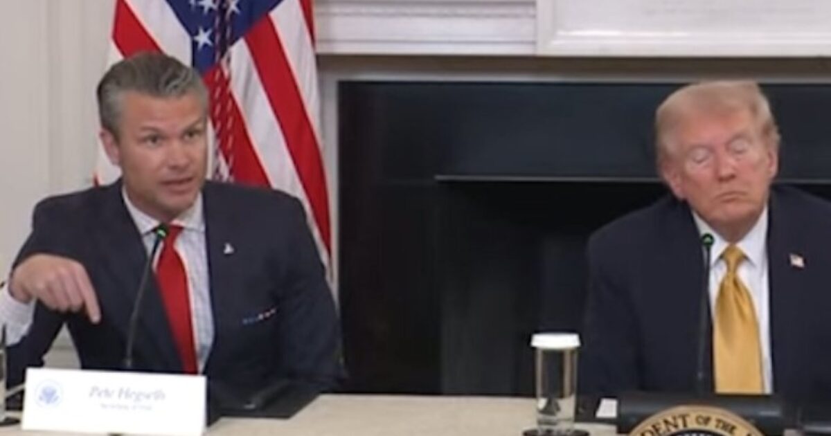 Pete Hegseth speaks during a discussion with former President Donald Trump at a roundtable event, featuring American flags in the background.
