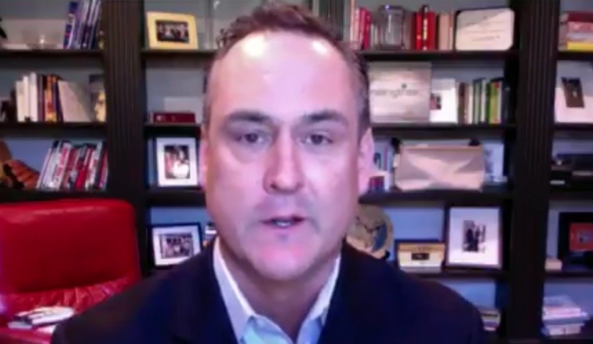 Professional man speaking from a home office, with bookshelves and framed photos in the background, highlighting a personal and engaging workspace.