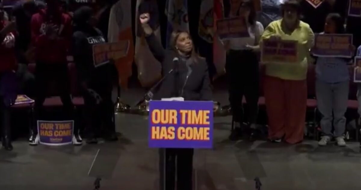 Speaker raising a fist at a rally, with supporters holding signs that read "Our Time Has Come," emphasizing themes of empowerment and social justice.