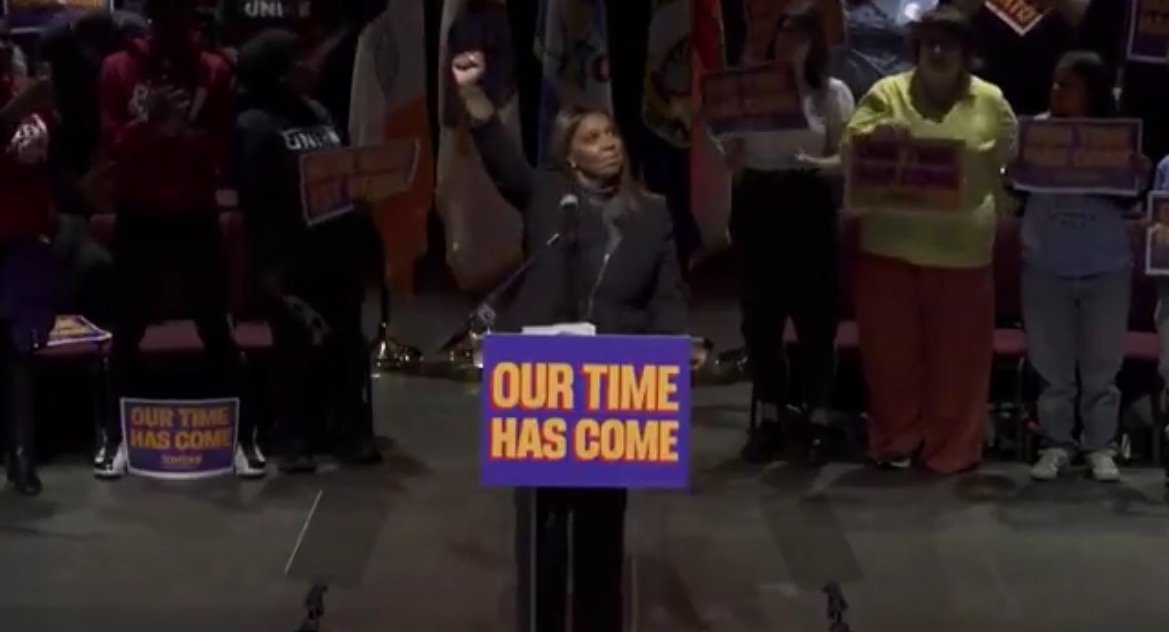Speaker raising a fist at a rally, with supporters holding signs that read "Our Time Has Come," emphasizing themes of empowerment and social justice.
