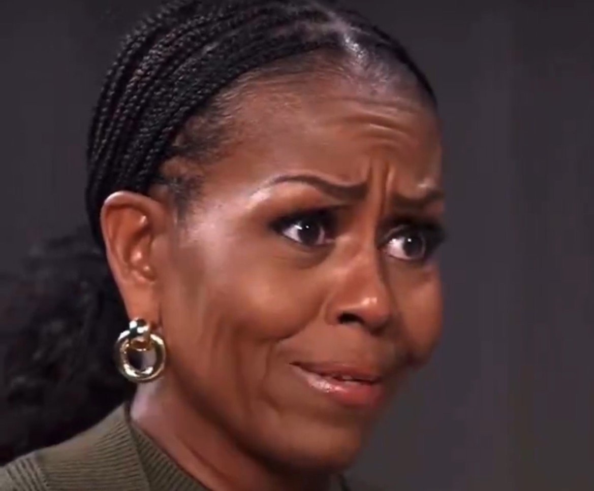 Close-up of a woman with braided hair, expressing emotion with a concerned facial expression, wearing large hoop earrings and a green top.