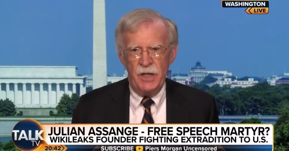 John Bolton discusses Julian Assange's fight against extradition to the U.S. during a live segment on Talk TV, with Washington D.C. landmarks in the background.