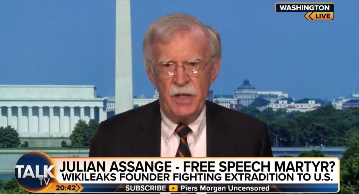 John Bolton discusses Julian Assange's fight against extradition to the U.S. during a live segment on Talk TV, with Washington D.C. landmarks in the background.