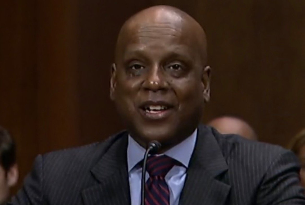 A smiling man in a suit speaks at a formal event, showcasing a confident demeanor during a Senate hearing.