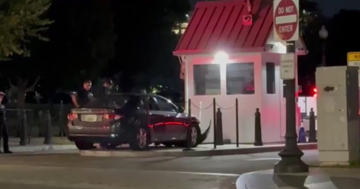 Police officers interact with a vehicle near a security booth at night, highlighting security measures in urban areas.