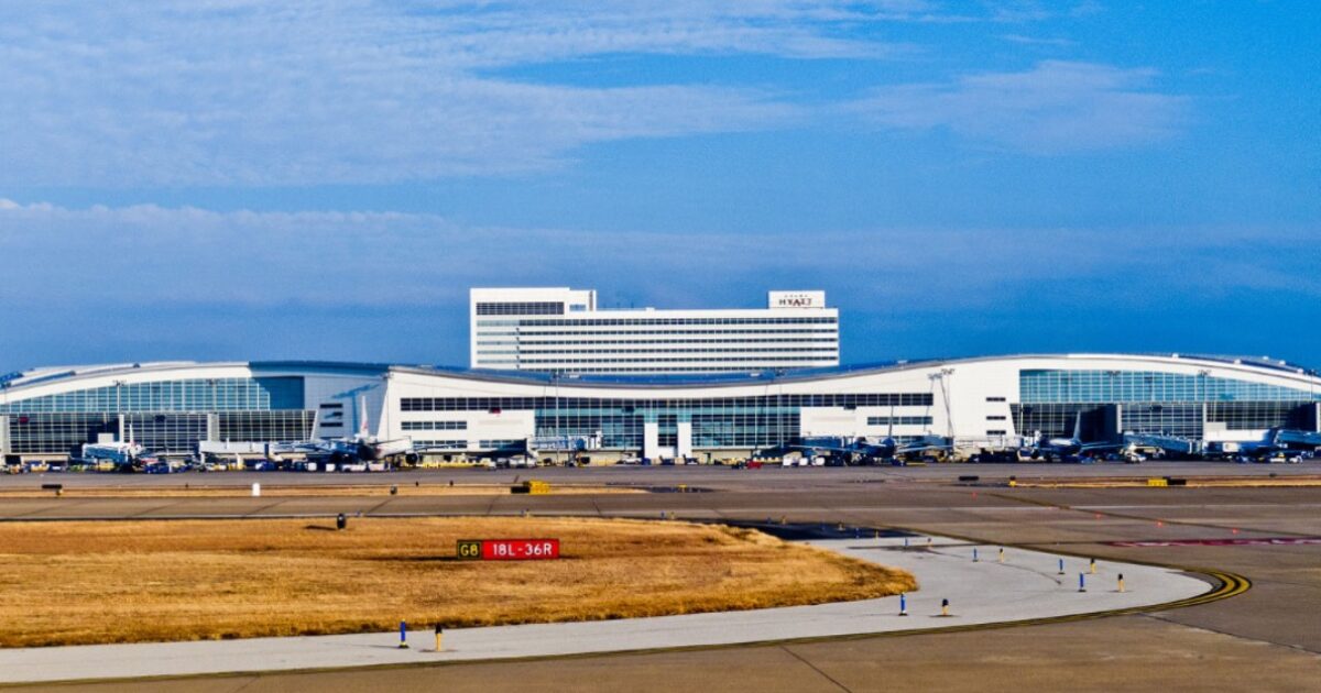 Modern airport terminal with multiple gates, aircraft parked on the tarmac, and a hotel in the background under a clear blue sky.